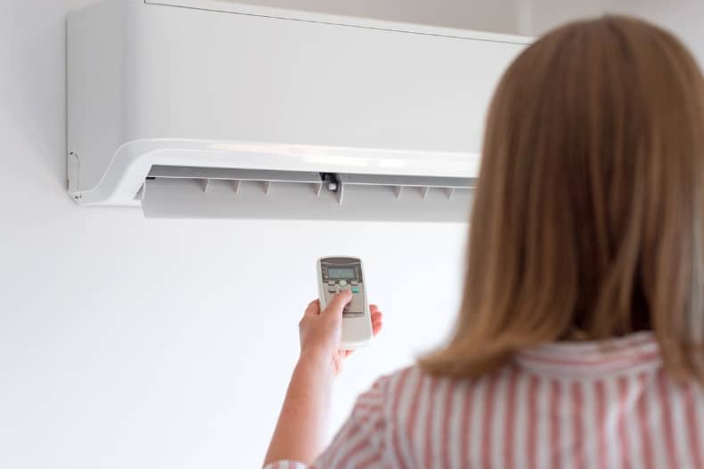 Woman Holding Remote Control Aimed At The Air Conditioner Picture Id859735208 1